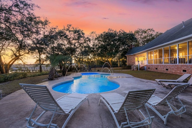 pool at dusk featuring pool water feature, a sunroom, a patio area, and a lawn