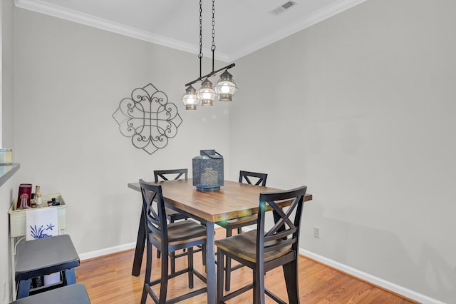 dining room featuring baseboards, visible vents, crown molding, and light wood finished floors