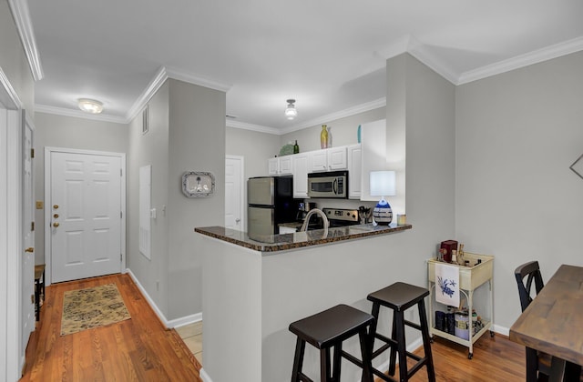 kitchen featuring appliances with stainless steel finishes, a breakfast bar, ornamental molding, and light wood-style flooring