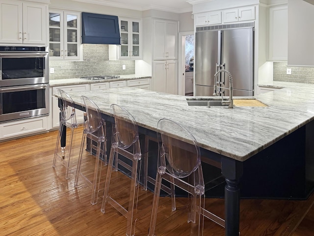 kitchen featuring white cabinetry, a kitchen breakfast bar, stainless steel appliances, and wall chimney exhaust hood