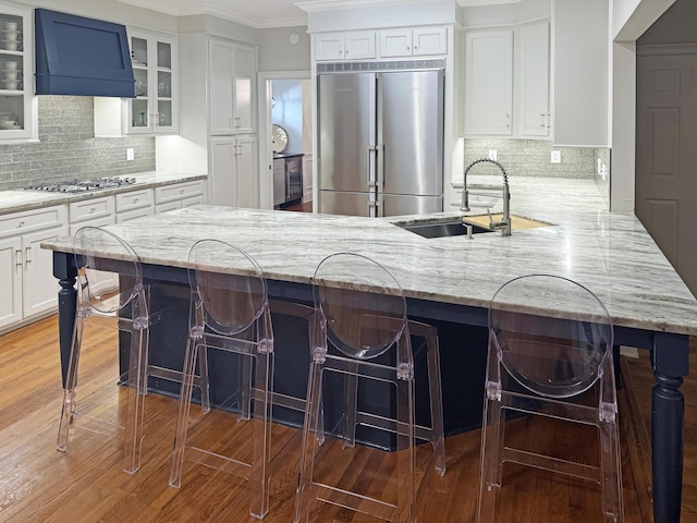 kitchen featuring a sink, white cabinets, glass insert cabinets, appliances with stainless steel finishes, and wall chimney range hood