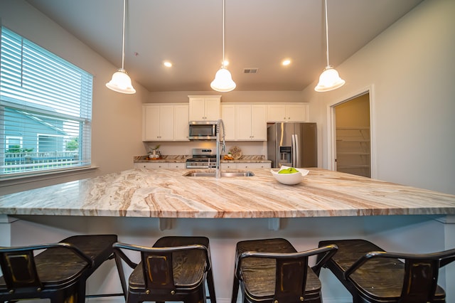 kitchen with white cabinets, stainless steel appliances, hanging light fixtures, and a breakfast bar area