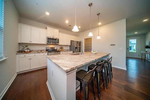 kitchen featuring white cabinets, pendant lighting, a center island with sink, appliances with stainless steel finishes, and dark wood-type flooring