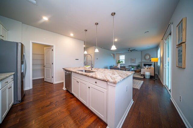 kitchen with ceiling fan, dark hardwood / wood-style flooring, light stone counters, a center island with sink, and appliances with stainless steel finishes