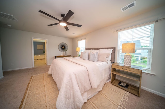 bedroom with light carpet, connected bathroom, multiple windows, and ceiling fan