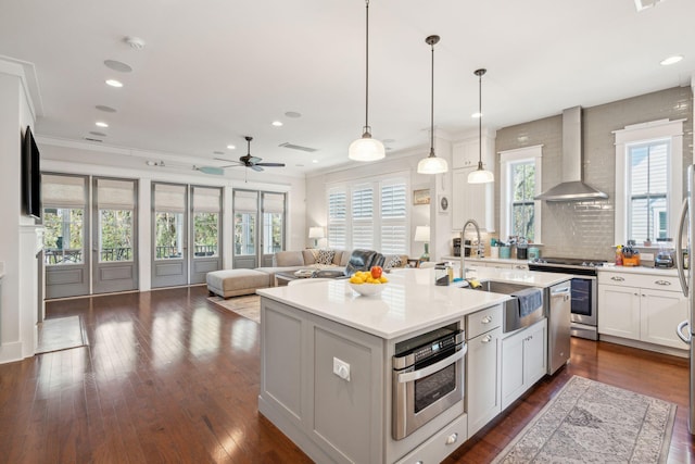 kitchen featuring dark wood-style floors, wall chimney exhaust hood, open floor plan, stainless steel appliances, and a sink