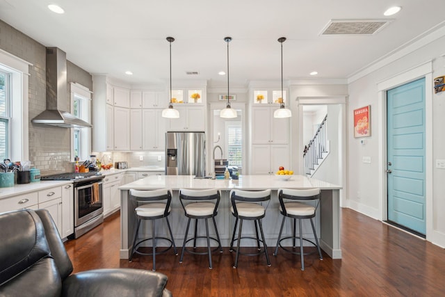 kitchen with stainless steel appliances, a sink, visible vents, light countertops, and wall chimney range hood