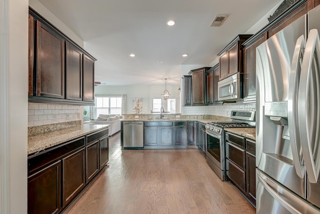 kitchen with appliances with stainless steel finishes, decorative light fixtures, light stone countertops, dark brown cabinets, and light wood-style floors