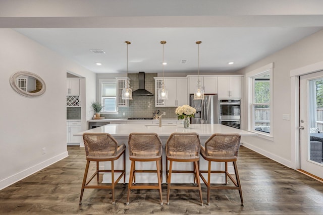 kitchen featuring dark wood-style flooring, appliances with stainless steel finishes, white cabinetry, wall chimney range hood, and tasteful backsplash