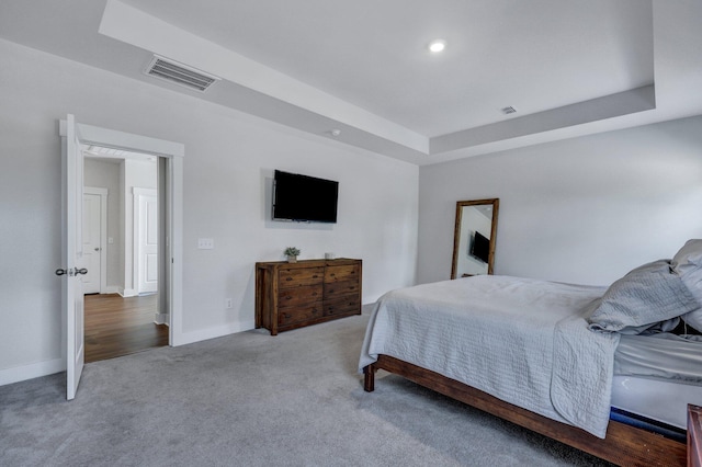 carpeted bedroom featuring a tray ceiling, visible vents, and baseboards