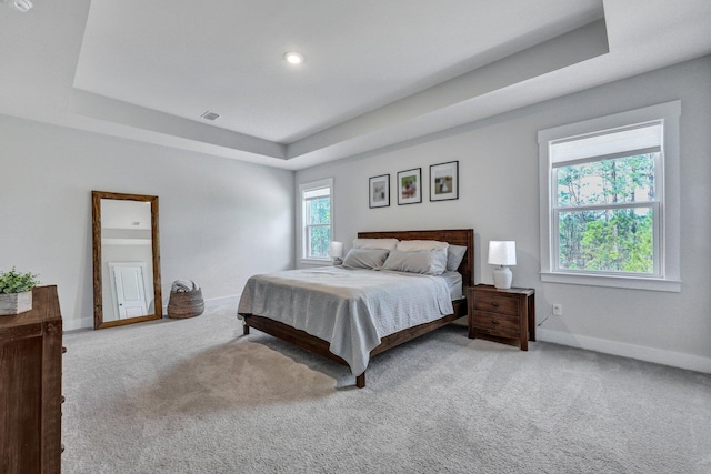 carpeted bedroom with a tray ceiling, baseboards, and visible vents