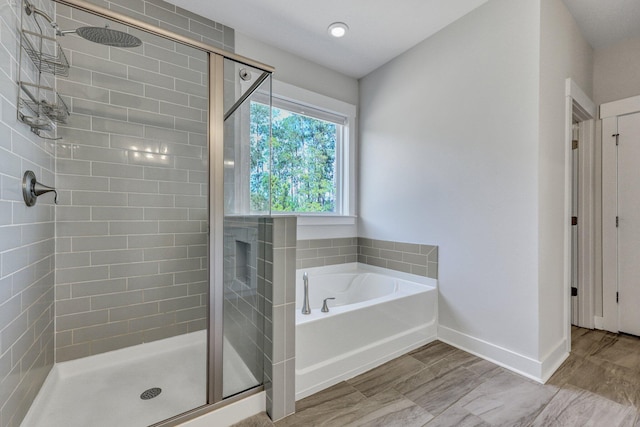 full bathroom with wood finished floors, baseboards, a bath, and a shower stall