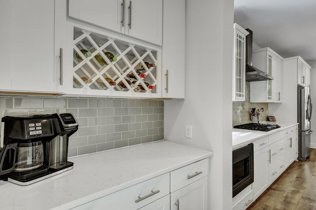 kitchen with white cabinetry, gas stovetop, stainless steel fridge, wall chimney exhaust hood, and built in microwave