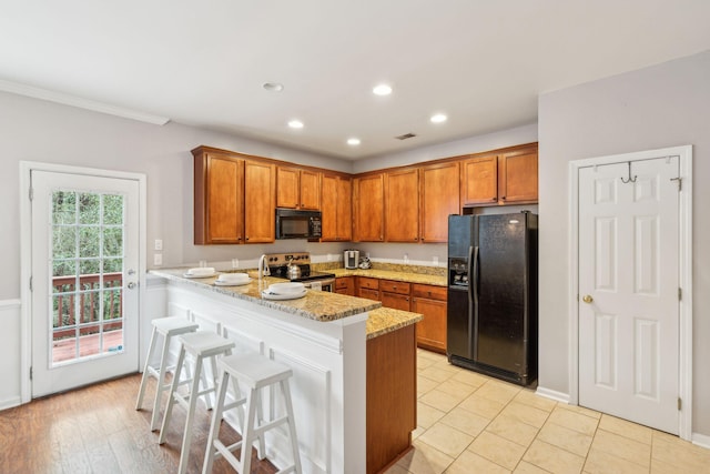 kitchen featuring brown cabinetry, a peninsula, black appliances, and a kitchen bar