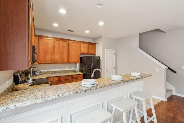 kitchen featuring visible vents, brown cabinets, black appliances, dark wood finished floors, and recessed lighting