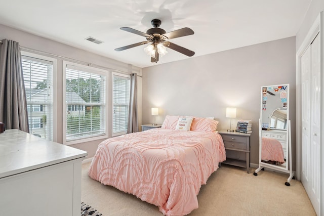 bedroom with visible vents, a ceiling fan, a closet, baseboards, and light colored carpet