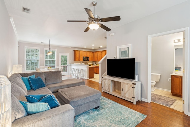 living area with a ceiling fan, wood finished floors, visible vents, baseboards, and ornamental molding