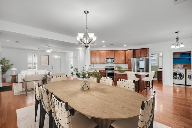 dining space featuring light wood-type flooring, ceiling fan with notable chandelier, sink, and independent washer and dryer