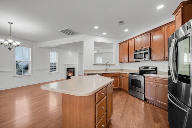 kitchen featuring hanging light fixtures, appliances with stainless steel finishes, sink, light wood-type flooring, and a center island