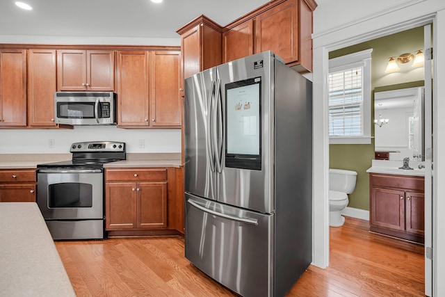 kitchen with appliances with stainless steel finishes, crown molding, and light wood-type flooring