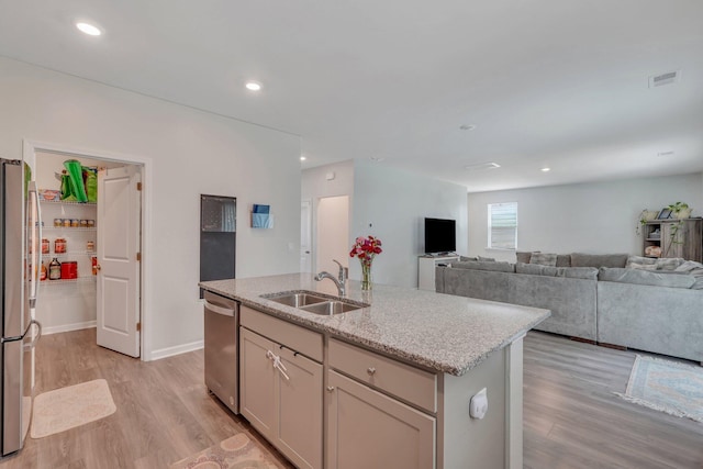 kitchen with a kitchen island with sink, sink, appliances with stainless steel finishes, light hardwood / wood-style floors, and light stone counters