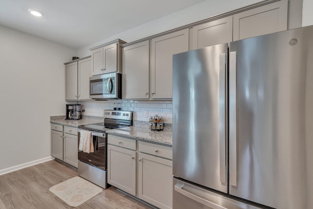 kitchen with decorative backsplash, appliances with stainless steel finishes, light stone countertops, gray cabinets, and light hardwood / wood-style floors