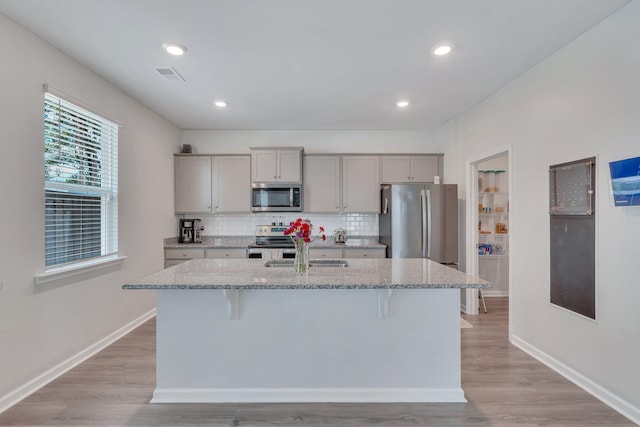 kitchen featuring stainless steel appliances, light stone counters, a kitchen bar, gray cabinets, and a kitchen island with sink