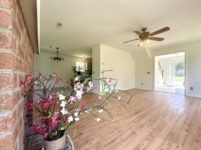 unfurnished living room with stairs, baseboards, wood finished floors, and ceiling fan with notable chandelier