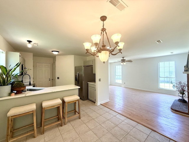 kitchen featuring stainless steel refrigerator with ice dispenser, visible vents, a sink, ceiling fan with notable chandelier, and light tile patterned flooring