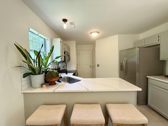 kitchen with a kitchen breakfast bar, stainless steel appliances, a peninsula, decorative backsplash, and visible vents