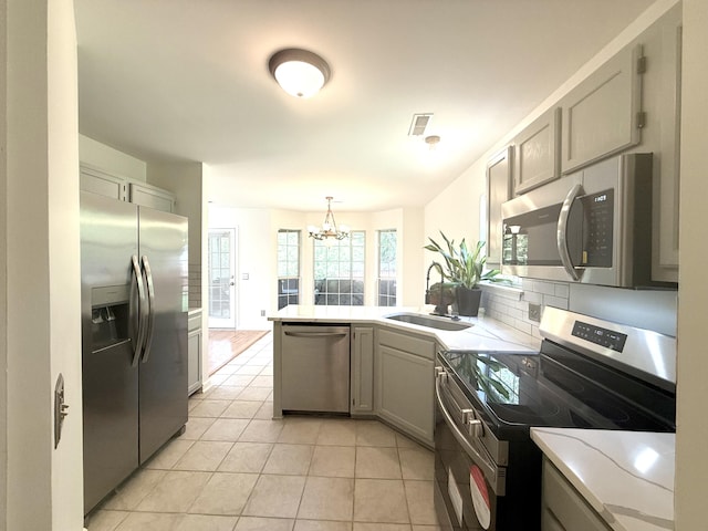 kitchen featuring appliances with stainless steel finishes, a sink, light countertops, a peninsula, and light tile patterned floors