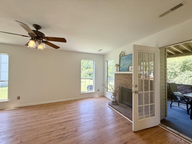 unfurnished living room featuring visible vents, wood finished floors, baseboards, a fireplace with raised hearth, and a ceiling fan