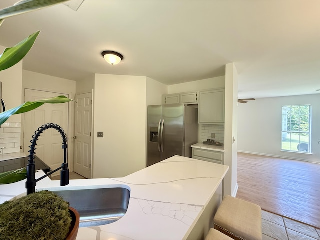 kitchen with stainless steel fridge, a sink, light countertops, light wood-type flooring, and tasteful backsplash