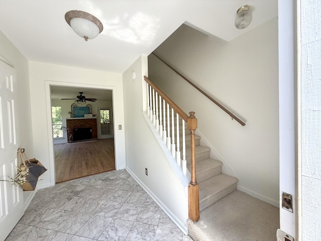 stairs featuring baseboards, marble finish floor, a brick fireplace, and ceiling fan