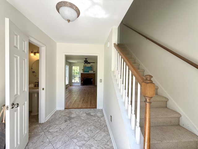 stairway with baseboards, marble finish floor, ceiling fan, and a fireplace