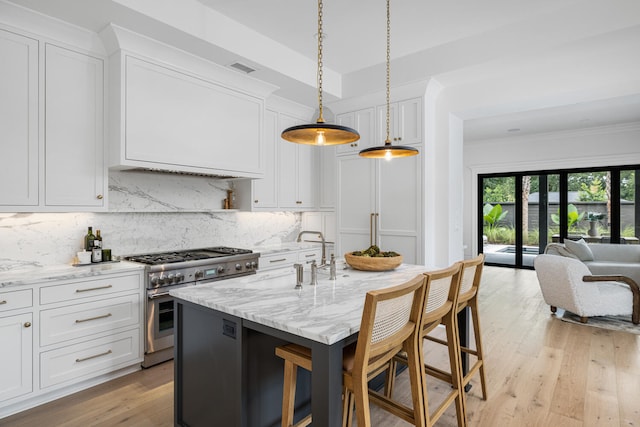 kitchen with high end stainless steel range, white cabinetry, light stone counters, decorative light fixtures, and a center island with sink