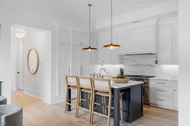 kitchen with white cabinetry, decorative light fixtures, high end stainless steel range, and an island with sink