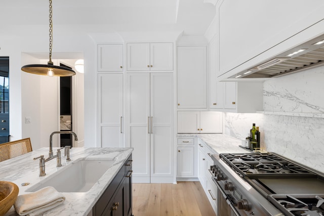 kitchen featuring sink, white cabinetry, stainless steel range, light stone countertops, and custom range hood