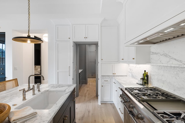 kitchen with sink, premium range hood, stainless steel gas range oven, light stone countertops, and white cabinets