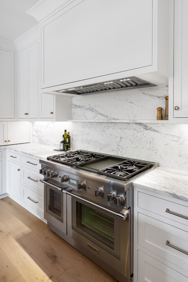 kitchen with backsplash, white cabinets, double oven range, light stone counters, and light wood-type flooring