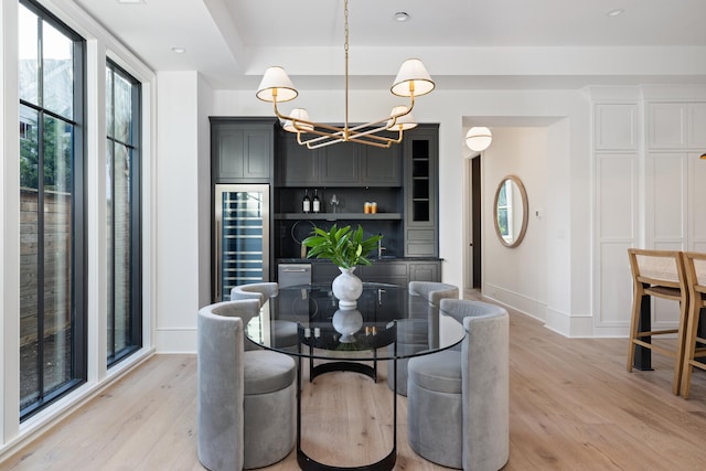 dining area featuring an inviting chandelier, light hardwood / wood-style floors, and beverage cooler