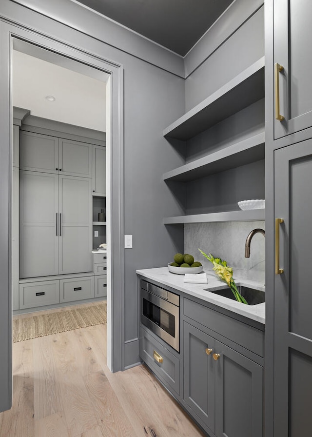 bar with stainless steel microwave, gray cabinets, sink, and light hardwood / wood-style flooring