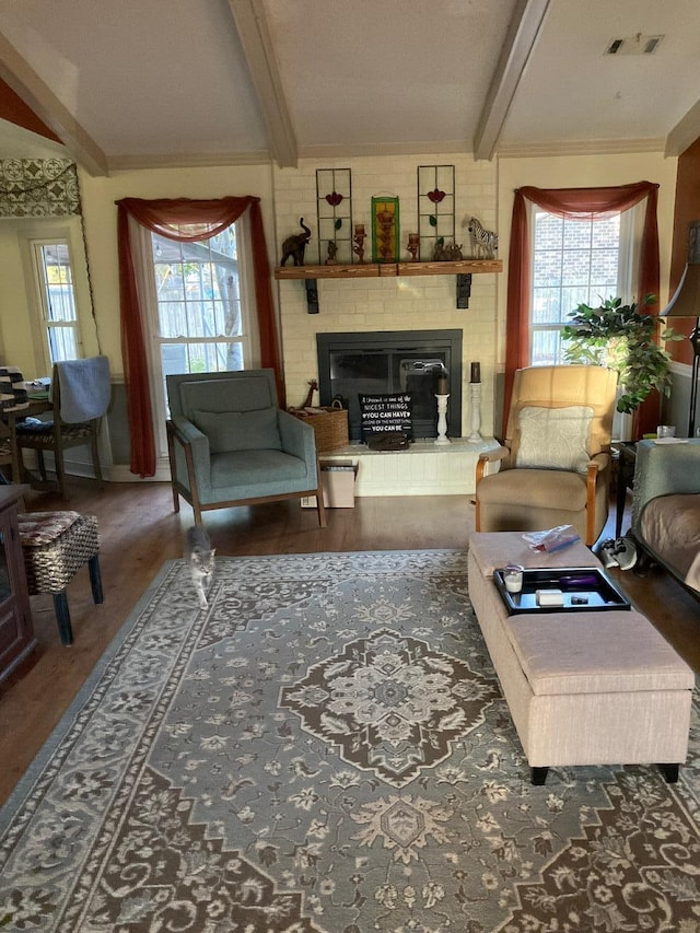 living room featuring beamed ceiling, dark wood-type flooring, a brick fireplace, and a healthy amount of sunlight