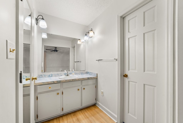 bathroom featuring hardwood / wood-style flooring, ceiling fan, vanity, and a textured ceiling