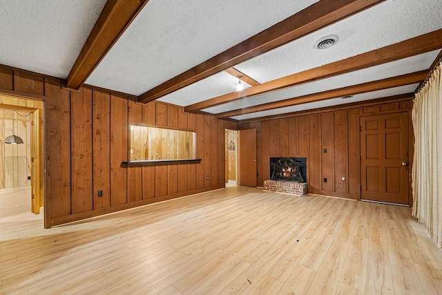 unfurnished living room featuring wood walls, light hardwood / wood-style floors, and a textured ceiling