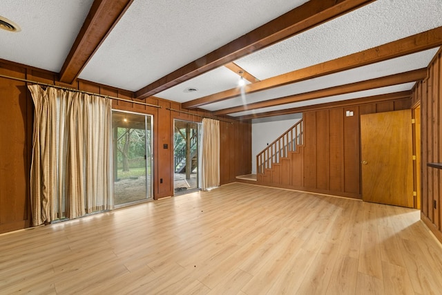 unfurnished living room with light hardwood / wood-style flooring, wooden walls, and a textured ceiling