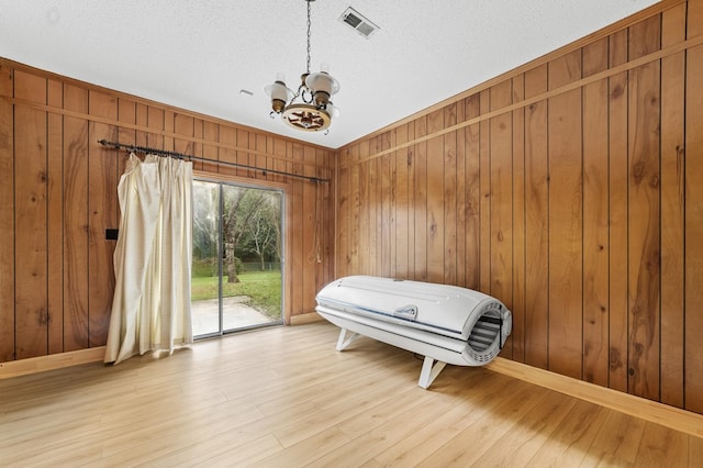 interior space with wood-type flooring, an inviting chandelier, wooden walls, and a textured ceiling