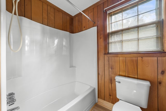 bathroom with hardwood / wood-style flooring, wooden walls, toilet, and washtub / shower combination