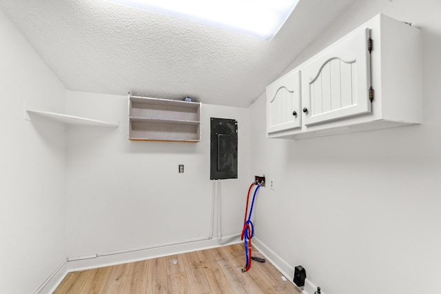 laundry room with electric panel, a textured ceiling, light hardwood / wood-style flooring, cabinets, and hookup for a washing machine