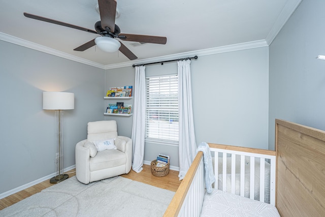 bedroom with a crib, ornamental molding, wood-type flooring, and ceiling fan